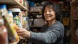© vadosloginov - A woman is smiling while reaching for a jar of food in a pantry. The pantry is filled with various food items, including a bottle of mustard. The woman is enjoying her time in the pantry