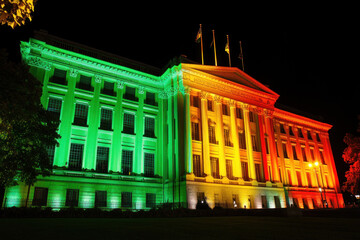 White house illuminated in green and red lights at night, symbolizing the holiday season with wreaths on every window.