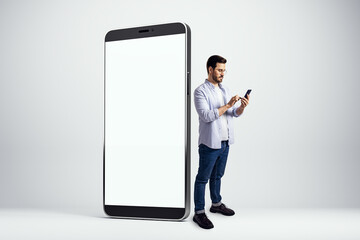 Fototapete - Man using smartphone beside a large blank screen mockup for presentation purposes.