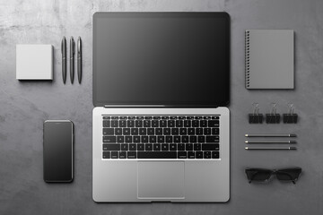 Wall Mural - Top view on blank dark screen of fully open modern laptop with black keyboard on dark grey surface with notebook, sunglasses, smartphone and office tools. 3D rendering, mockup