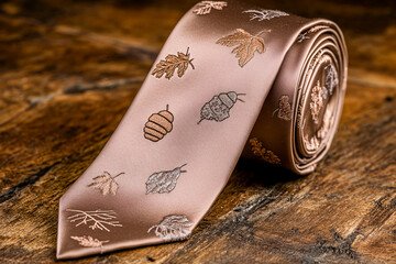 A Thanksgiving tie adorned with embroidered acorns and maple leaves is styled on a rustic table surrounded by fall decor