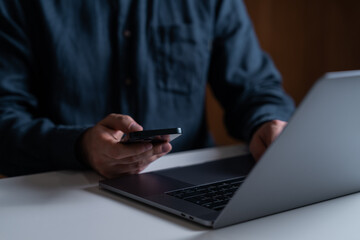 Man using smartphone, typing on the laptop keyboard on desk