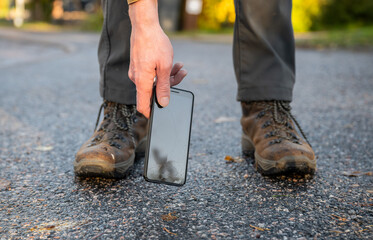 Close-up of man in boots picking up his broken smartphone with cracked screen glass