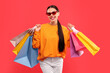 © New Africa - Smiling woman with colorful shopping bags on red background