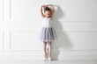 © New Africa - Little ballerina practicing dance moves near white wall indoors