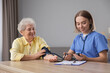 © New Africa - Healthcare worker measuring patient's blood pressure at wooden table indoors