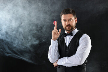 Poster - Croupier holding casino chip on black background with smoke, space for text