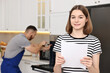 © New Africa - Smiling woman with sheet of paper and repairman fixing oven in kitchen, selective focus