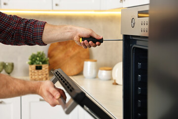 Poster - Repairman with screwdriver fixing oven in kitchen, closeup