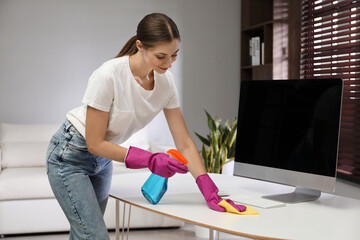 Poster - Young woman cleaning table with rag and spray in office