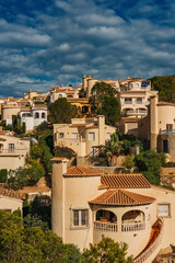 Wall Mural - Spanish residential area on a slope of a hill with green vegetation under blue sky with fluffy clouds.