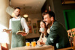 © BGStock72 - Waiter serves delicious vegetarian dishes to cheerful diners in a vibrant café during a sunny afternoon