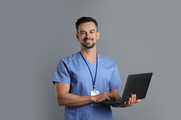 Canvas Print - Smiling nurse with badge and laptop on grey background