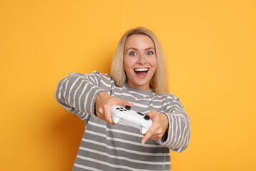 Happy woman playing video games with controller on orange background