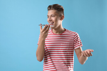 Poster - Young man recording voice message via smartphone on light blue background