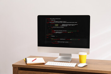 Programmer's workplace. Modern compter with unfinished code, paper cup of drink and stationery on desk indoors