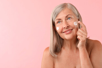 Sticker - Senior woman applying face cream on pink background. Space for text