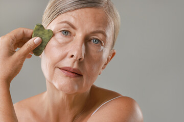 Poster - Beautiful woman doing facial massage with gua sha tool on grey background, closeup