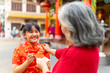 © CandyRetriever  - Chinese lunar new year traditional holiday festival celebration concept. Happy Asian family grandmother giving money gift in red envelopes and blessing to little grandchild girl in Chinese red dress.