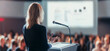 © KAMAPAN - Female speaker giving a talk on corporate business conference. Unrecognizable people in audience at conference hall. Business and Entrepreneurship event