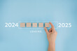 © olyphotostories - 2025 New Year Loading. Female hand moving wooden blocks with Loading bar between 2024 and 2025 on a blue background. Concept for transition, progress, new year, and future plans