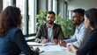 © Chahal - A middle-aged Caucasian man with short dark hair and a beard wearing a suit, sitting at a table in an office environment and discussing documents with other people