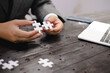 © Worapon - Businessman sitting at a table intently completing a jigsaw puzzle, demonstrating problem-solving, strategic thinking, and business decision-making, as well as attention to detail and patience.