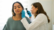 © AntonioDiaz - Female doctor wearing gloves is using an otoscope to examine the ear of a young woman in a medical office