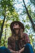© StockUp - Young woman in casual attire looks up in a tranquil forest, wearing a hat, expressing connection with nature.