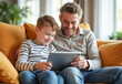 © Radorog. - father and son are sitting on the couch looking at a tablet and laughing