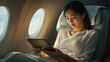 © Johannes - Asian woman working and planning on an airplane. Asian woman using digital tablet while sitting on an airplane.