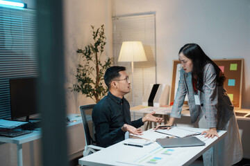 Two business colleagues having a disagreement while working together at a desk in an office at night