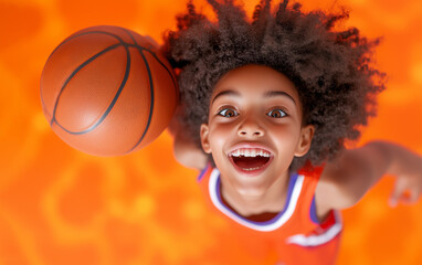 Excited child with curly hair playing basketball on an orange court during daytime fun