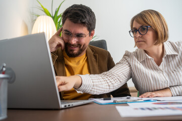 Colleagues in a business meeting discussing project details, collaborating over a laptop. Professional teamwork, consultation, and planning in an office environment.