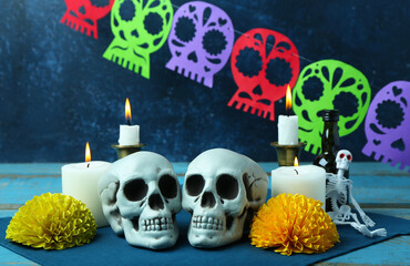 Painted skulls for Mexico's Day of the Dead (El Dia de Muertos) and glowing candles on blue wooden table