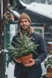© Iryna - A man is holding a potted plant in a snow-covered area. He is wearing a blue jacket and a brown hat