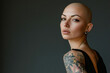 © kristina - Woman with bald hair and tattoos looking out at ocean waves crashing against rocks, under cloudy sky.