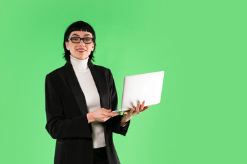 Professional woman in a black suit standing with a laptop against a bright green background