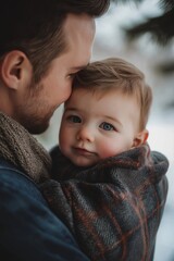 A father lovingly holds his baby wrapped in a cozy blanket, capturing a tender and intimate fatherhood moment in soft light.