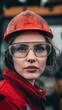 © h3design - Young woman in a red work jacket and helmet with protective glasses at a construction site during daylight hours