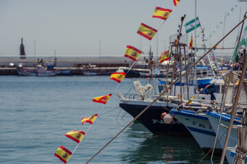 A boat on a sea pier with many Spanish flags flying. Boats and launches with Spanish flags are moored to the pier