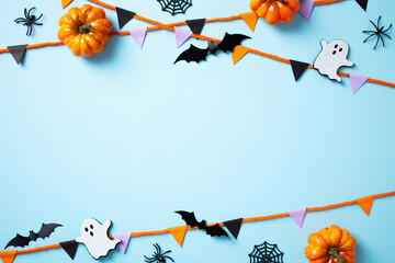 Frame of Halloween decorations, pumpkins, bats, ghosts, and spiders on a light blue background. Flat lay, top view, copy space.