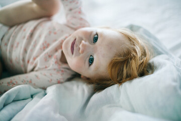 Aesthetic minimalistic Portrait of a cute happy ginger-haired blue-eyed baby girl in pyjamas after her nap