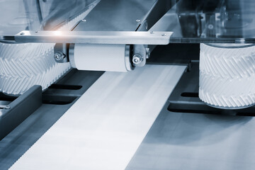 Poster - A conveyor belt is transporting a white roll of paper. The belt is moving the paper along its length, and it is in a factory setting