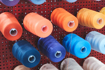 Aufkleber - A row of colorful spools of thread hanging on a red wall. The spools are of different colors and sizes, and they are arranged in a neat and orderly fashion