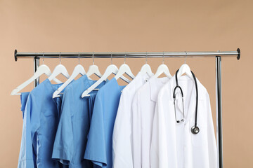 Wall Mural - Different medical workers' uniforms and stethoscope on clothing rack against beige background