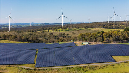 Wall Mural - aerial drone view of a hybrid solar and wind farm showing the large wind turbines in the background 