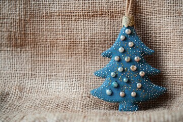 Wall Mural - Handmade blue textile cotton fabric naive retro style Christmas tree ornament decorated with beads on burlap background, copy space background - generative ai