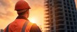 © Pakkarada - Construction worker observing sunset at building site, wearing safety gear.