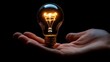 © loxia stock image - A glowing light bulb held in a hand against a black background.